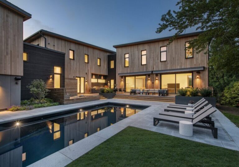 Daytime view of super-insulated rectangular pool with surrounding deck and lounge chairs, Zero Energy Design home.